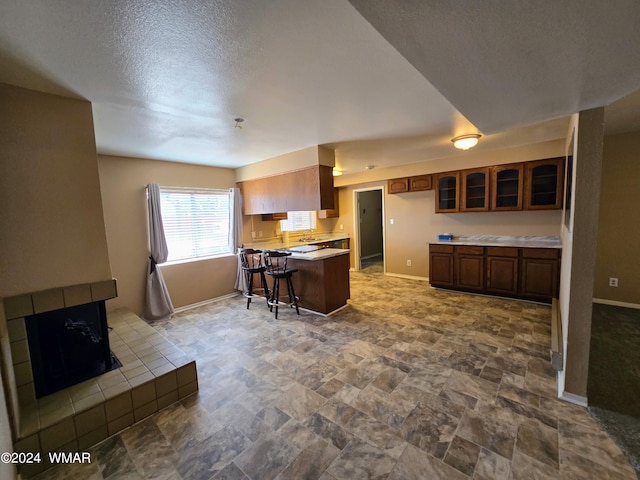 kitchen with a tile fireplace, baseboards, light countertops, a kitchen bar, and glass insert cabinets