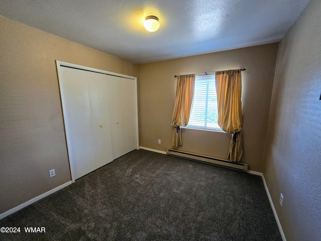 unfurnished bedroom with a closet, baseboards, dark carpet, and baseboard heating