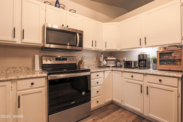 kitchen with appliances with stainless steel finishes, wood finished floors, white cabinets, vaulted ceiling, and light stone counters