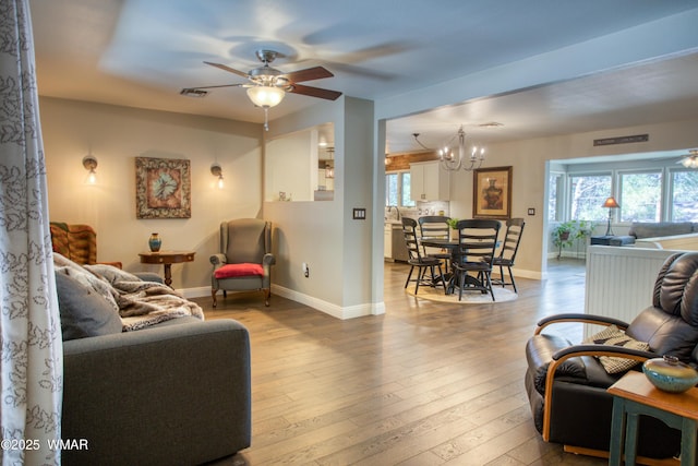 living room with hardwood / wood-style flooring, baseboards, visible vents, and ceiling fan with notable chandelier