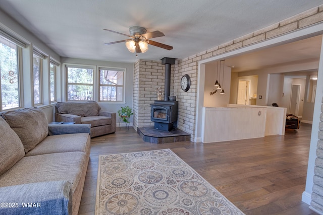 living area featuring ceiling fan, wood finished floors, and a wood stove
