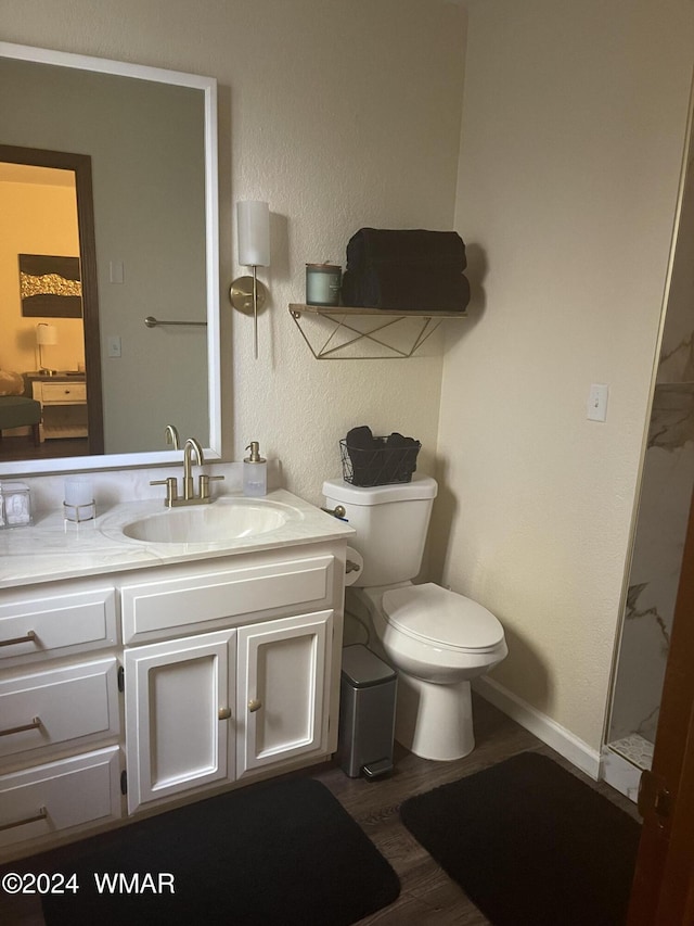 bathroom featuring wood finished floors, vanity, walk in shower, baseboards, and toilet