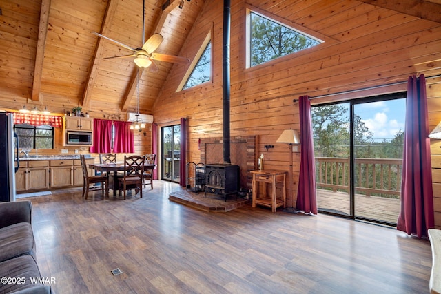 living area featuring wooden walls, wooden ceiling, wood finished floors, beamed ceiling, and a wood stove