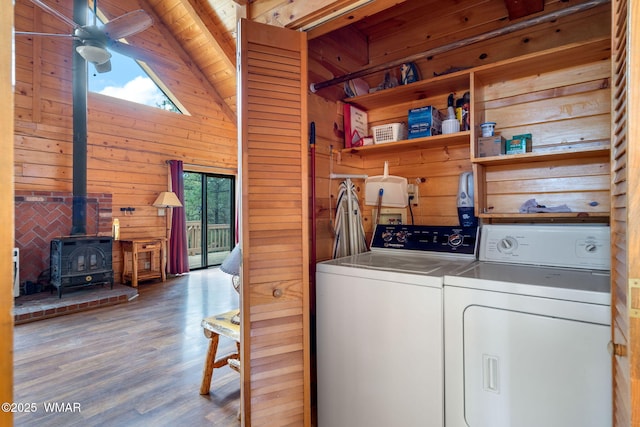 laundry room featuring laundry area, wooden walls, washer and clothes dryer, ceiling fan, and a wood stove