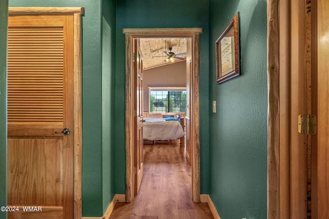 corridor featuring baseboards, vaulted ceiling, and light wood finished floors