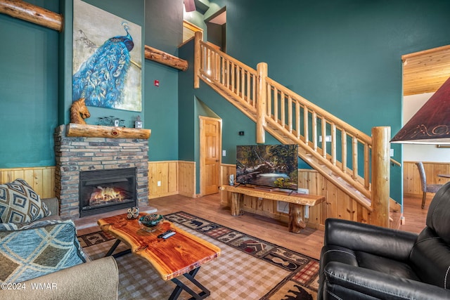 living room with a towering ceiling, wood finished floors, a stone fireplace, wainscoting, and stairs