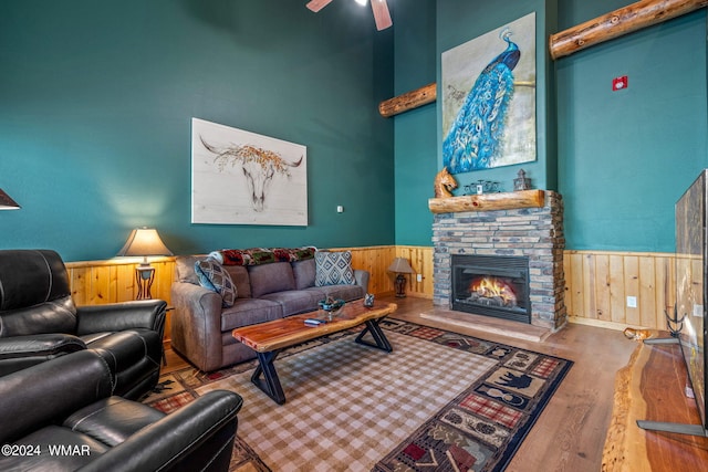 living room featuring wood finished floors, a wainscoted wall, a stone fireplace, and wooden walls
