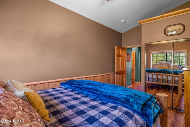 bedroom featuring wainscoting, vaulted ceiling, wood walls, and wood finished floors
