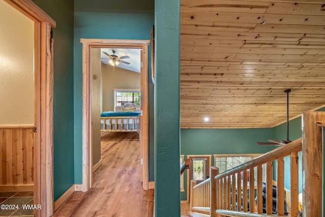 hallway with an upstairs landing, lofted ceiling, wood finished floors, wood ceiling, and wooden walls
