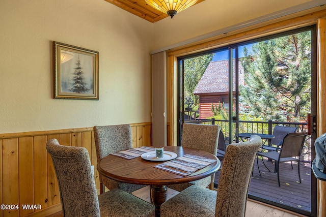 dining space with light wood finished floors, wooden ceiling, a wainscoted wall, and wood walls