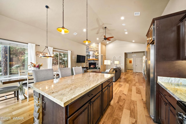 kitchen with light wood finished floors, ceiling fan, decorative light fixtures, dark brown cabinetry, and a stone fireplace
