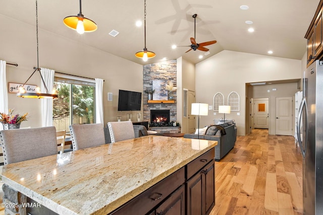 kitchen with visible vents, light wood-style flooring, a ceiling fan, freestanding refrigerator, and a stone fireplace