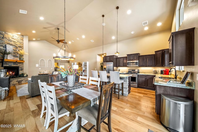 dining space featuring visible vents, light wood-style flooring, high vaulted ceiling, and a stone fireplace