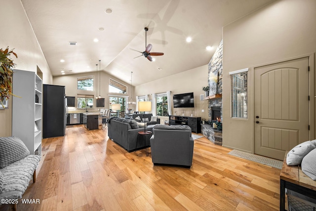 living area featuring plenty of natural light, a fireplace, light wood-style floors, and a ceiling fan