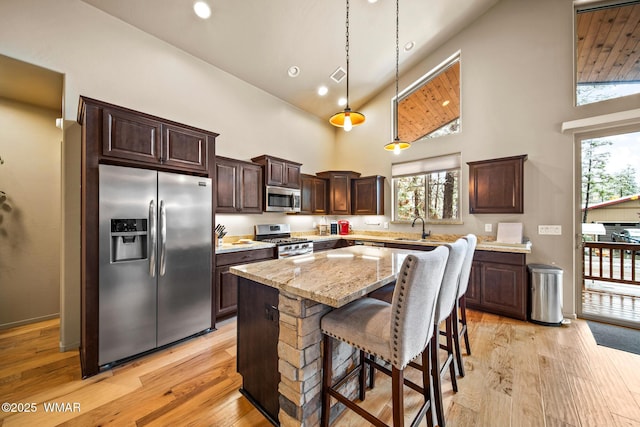 kitchen with dark brown cabinets, appliances with stainless steel finishes, a kitchen island, and light wood-type flooring