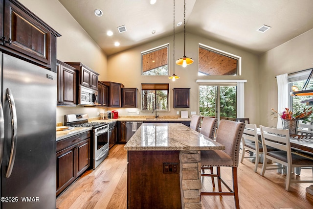 kitchen with a center island, stainless steel appliances, dark brown cabinetry, a breakfast bar area, and light wood finished floors