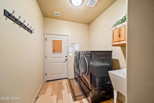 laundry room with light wood finished floors, visible vents, washer and clothes dryer, cabinet space, and a sink