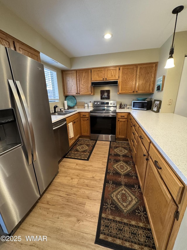 kitchen with light wood-style flooring, brown cabinets, stainless steel appliances, light countertops, and under cabinet range hood