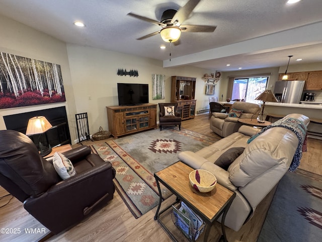 living area featuring light wood-type flooring, ceiling fan, a textured ceiling, and recessed lighting