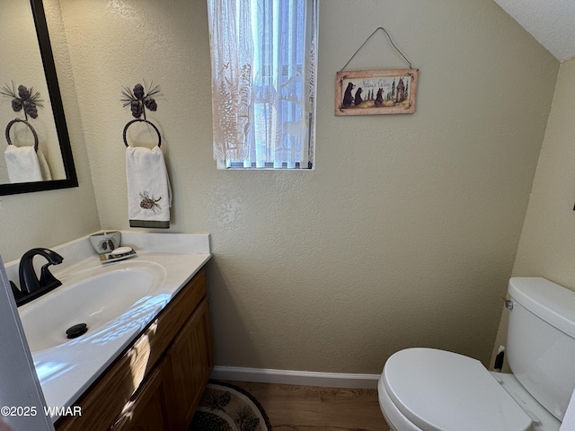 bathroom featuring toilet, baseboards, wood finished floors, and vanity