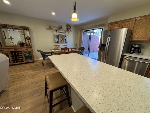 kitchen featuring light wood-style flooring, stainless steel appliances, hanging light fixtures, light countertops, and a kitchen bar