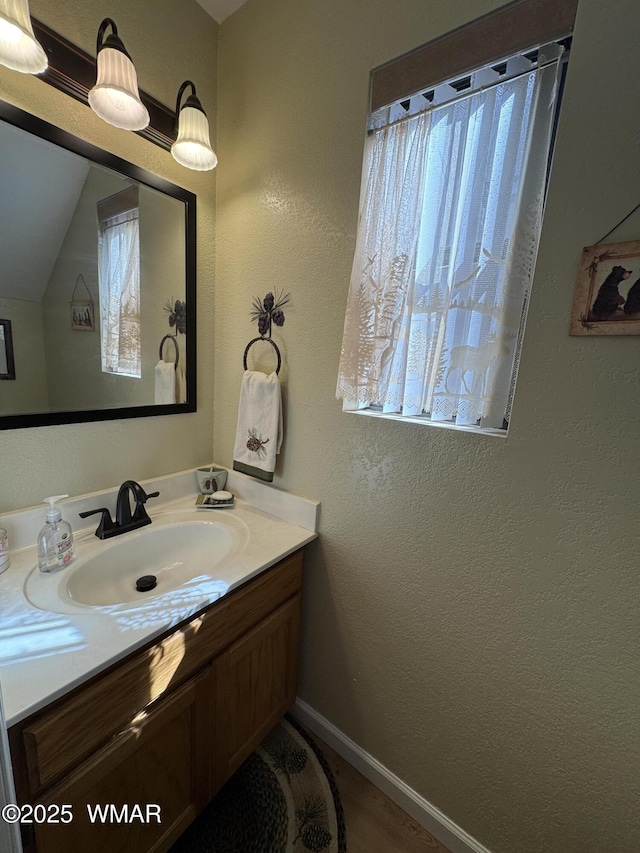 bathroom with a textured wall, baseboards, and vanity