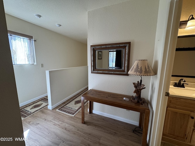 corridor featuring a textured ceiling, baseboards, a sink, and wood finished floors