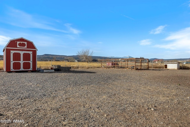 view of yard featuring an outbuilding, a storage unit, a mountain view, fence, and a rural view