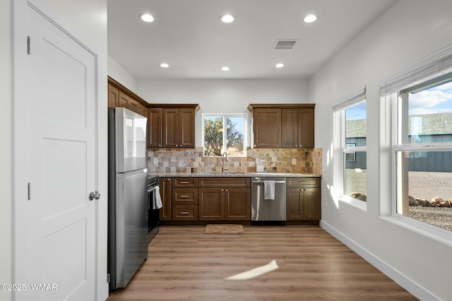 kitchen featuring visible vents, decorative backsplash, appliances with stainless steel finishes, light wood-type flooring, and a sink