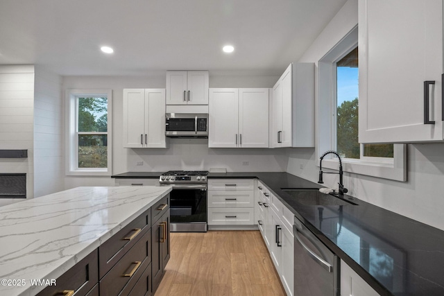 kitchen featuring white cabinetry, light stone counters, a sink, light wood-style flooring, and stainless steel appliances