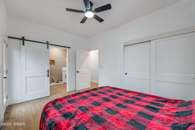 bedroom featuring a ceiling fan, a barn door, baseboards, a closet, and light wood-style flooring