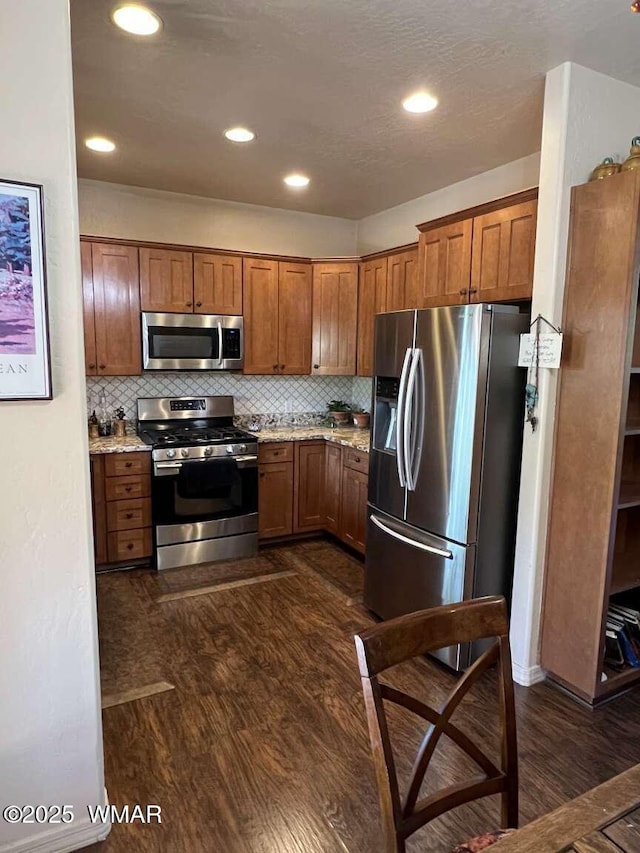 5380 Branding Iron Loop, Pinetop, AZ 85935 - kitchen featuring appliances with stainless steel finishes, brown cabinetry, dark wood-style floors, tasteful backsplash, and light stone counters