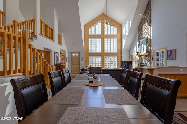 dining space featuring high vaulted ceiling, ceiling fan, and stairs