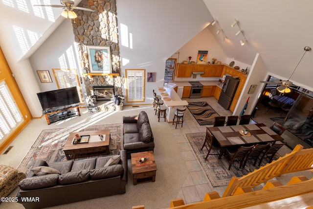 living room with light tile patterned floors, high vaulted ceiling, ceiling fan, a stone fireplace, and track lighting