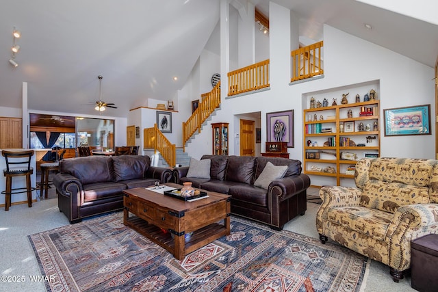 living area featuring high vaulted ceiling, carpet flooring, a ceiling fan, and stairs