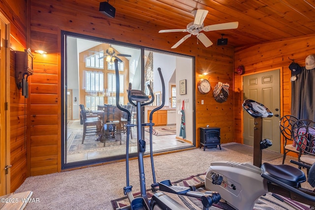 exercise room with wooden walls, carpet, ceiling fan, wooden ceiling, and a wood stove