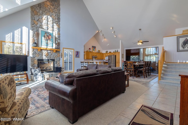 living room with ceiling fan, stairs, light tile patterned floors, a fireplace, and high vaulted ceiling