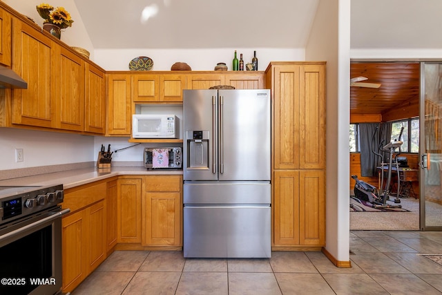 kitchen with stainless steel appliances, light tile patterned flooring, brown cabinetry, light countertops, and lofted ceiling