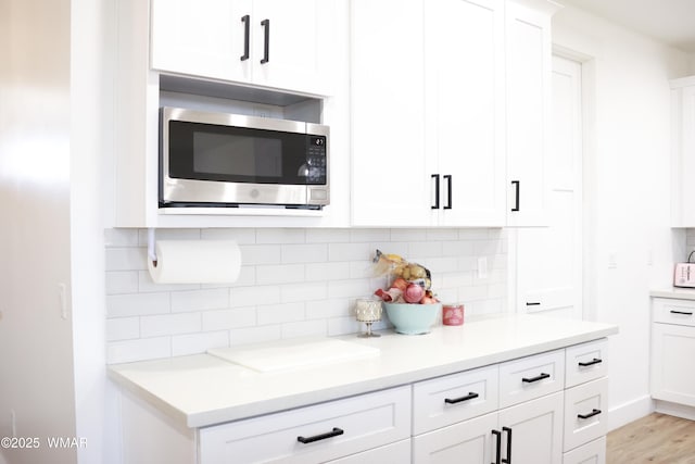 kitchen featuring light countertops, white cabinets, stainless steel microwave, and backsplash