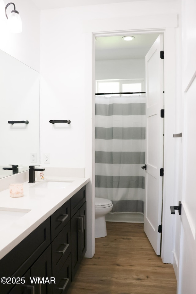 full bathroom with double vanity, a shower with shower curtain, toilet, wood finished floors, and a sink