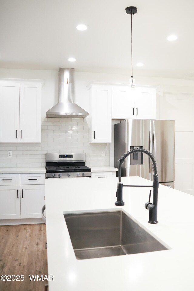 kitchen with wall chimney exhaust hood, appliances with stainless steel finishes, a sink, and decorative backsplash