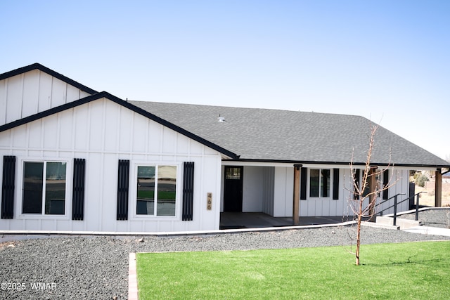 view of front of property featuring roof with shingles, a front lawn, and board and batten siding