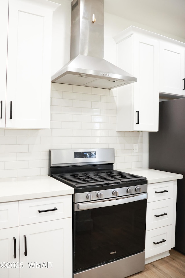 kitchen with wall chimney exhaust hood, stainless steel range with gas cooktop, white cabinetry, and light countertops