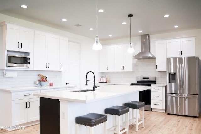 kitchen with light countertops, light wood-style flooring, appliances with stainless steel finishes, a sink, and wall chimney exhaust hood