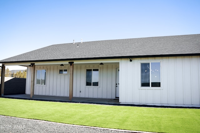 rear view of house featuring a yard, board and batten siding, a patio, and roof with shingles