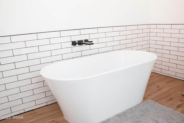 bathroom featuring a freestanding bath, tile walls, and wood finished floors