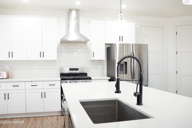 kitchen featuring stainless steel appliances, a sink, white cabinets, light countertops, and wall chimney exhaust hood