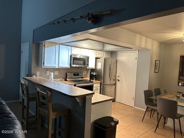 kitchen featuring light countertops, appliances with stainless steel finishes, white cabinetry, a peninsula, and a kitchen breakfast bar