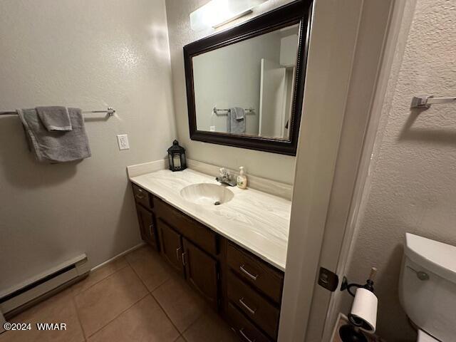 bathroom featuring a textured wall, toilet, a baseboard heating unit, vanity, and tile patterned floors