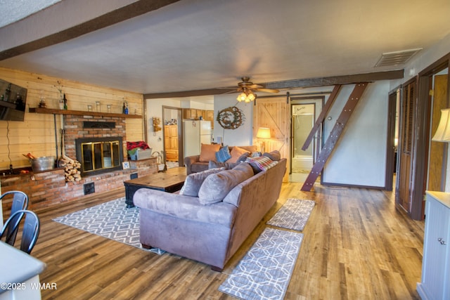 living area featuring visible vents, a barn door, a brick fireplace, a ceiling fan, and wood finished floors